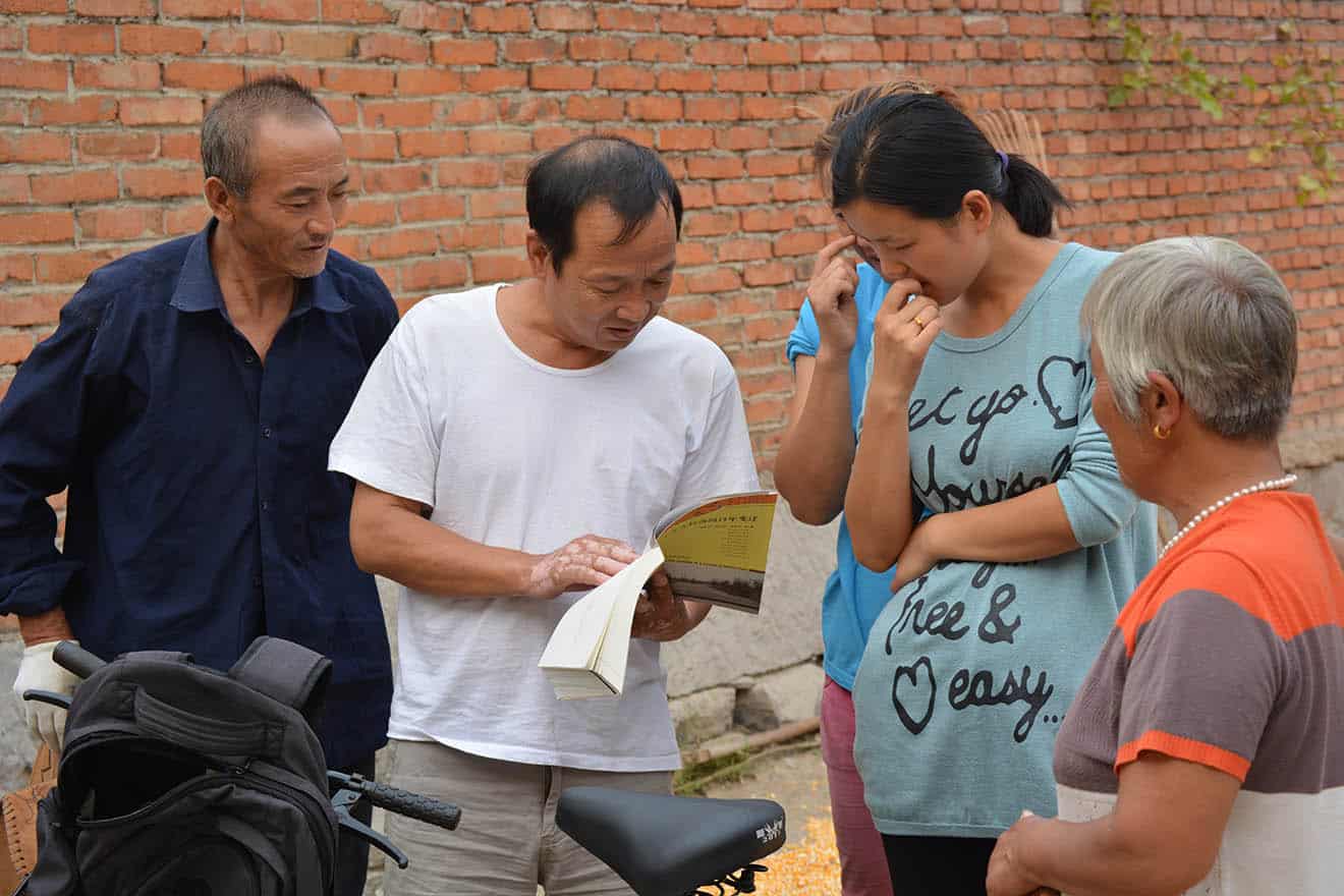 Man with a bike is standing holding a book, four other people looking down at it.